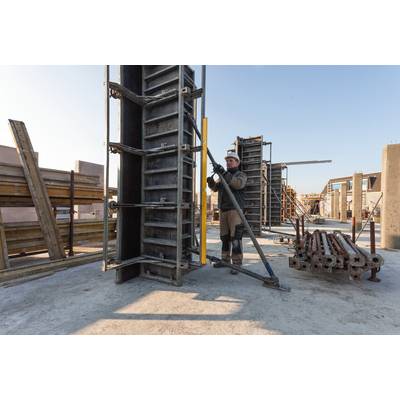 Ein Bauarbeiter befestigt eine Schalungsstütze an einer Betonform auf einer Baustelle. Um ihn herum stehen verschiedene Bauformen.