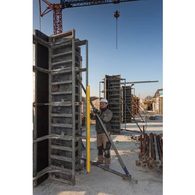 Arbeiter auf Baustelle richtet Schalung aus. Metallgerüste und Kran im Hintergrund. Klarer Himmel signalisiert gutes Wetter.