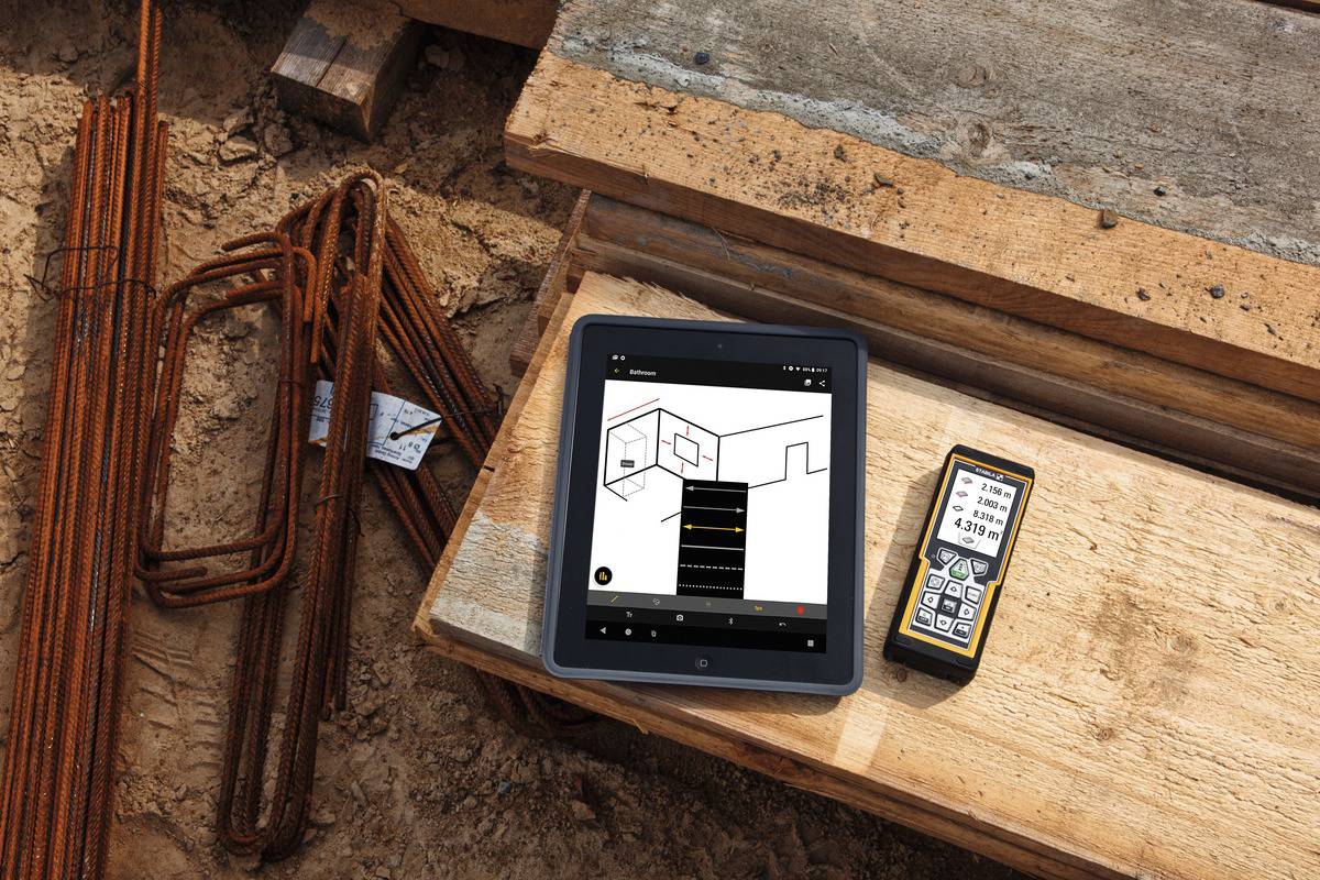 Ein Tablet und ein digitales Messgerät liegen auf einer Baustelle. Das Tablet zeigt eine Bauzeichnung, das Messgerät eine Messung an.