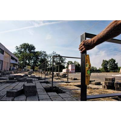Eine Baustelle mit einem Arbeiter, der ein Gestell ausrichtet. Im Hintergrund sind Gebäude und Bäume zu sehen.