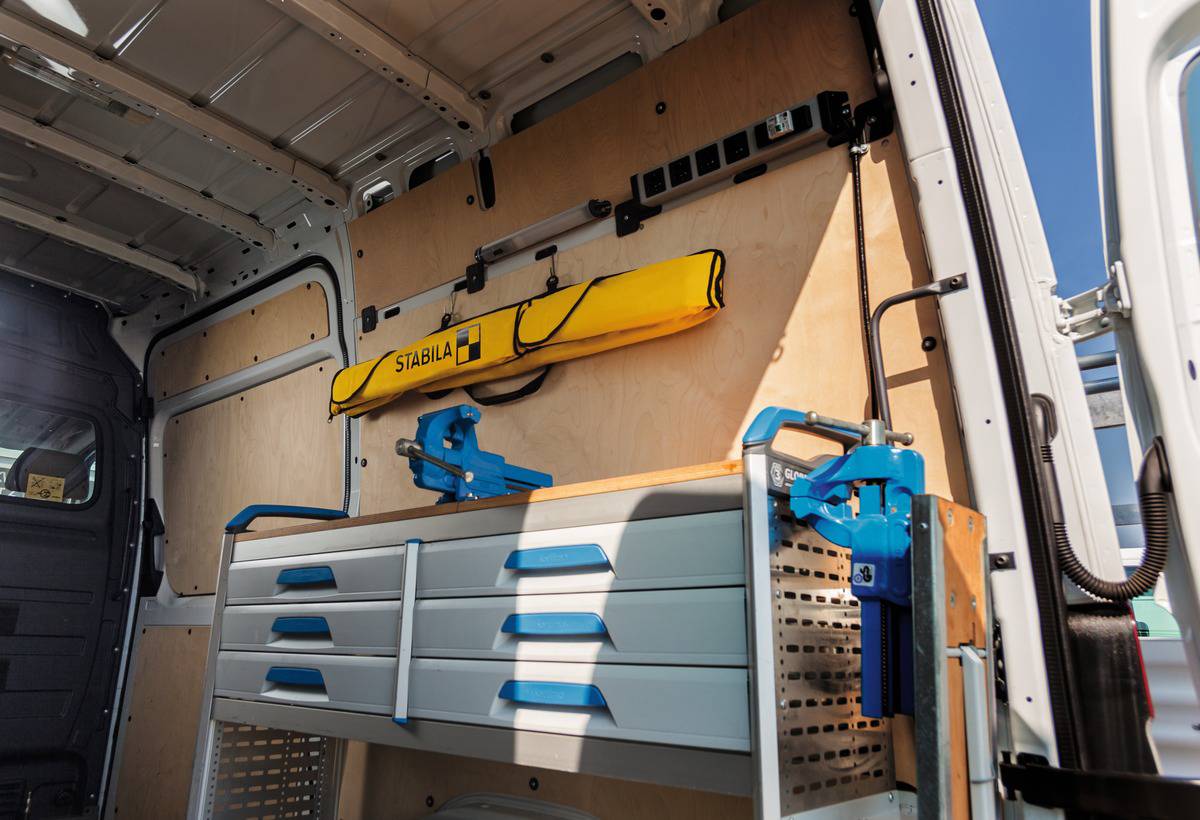 Innenraum eines Transporters mit gelben und blauen Werkzeugen an der Wand montiert; graue Schubladen darunter.