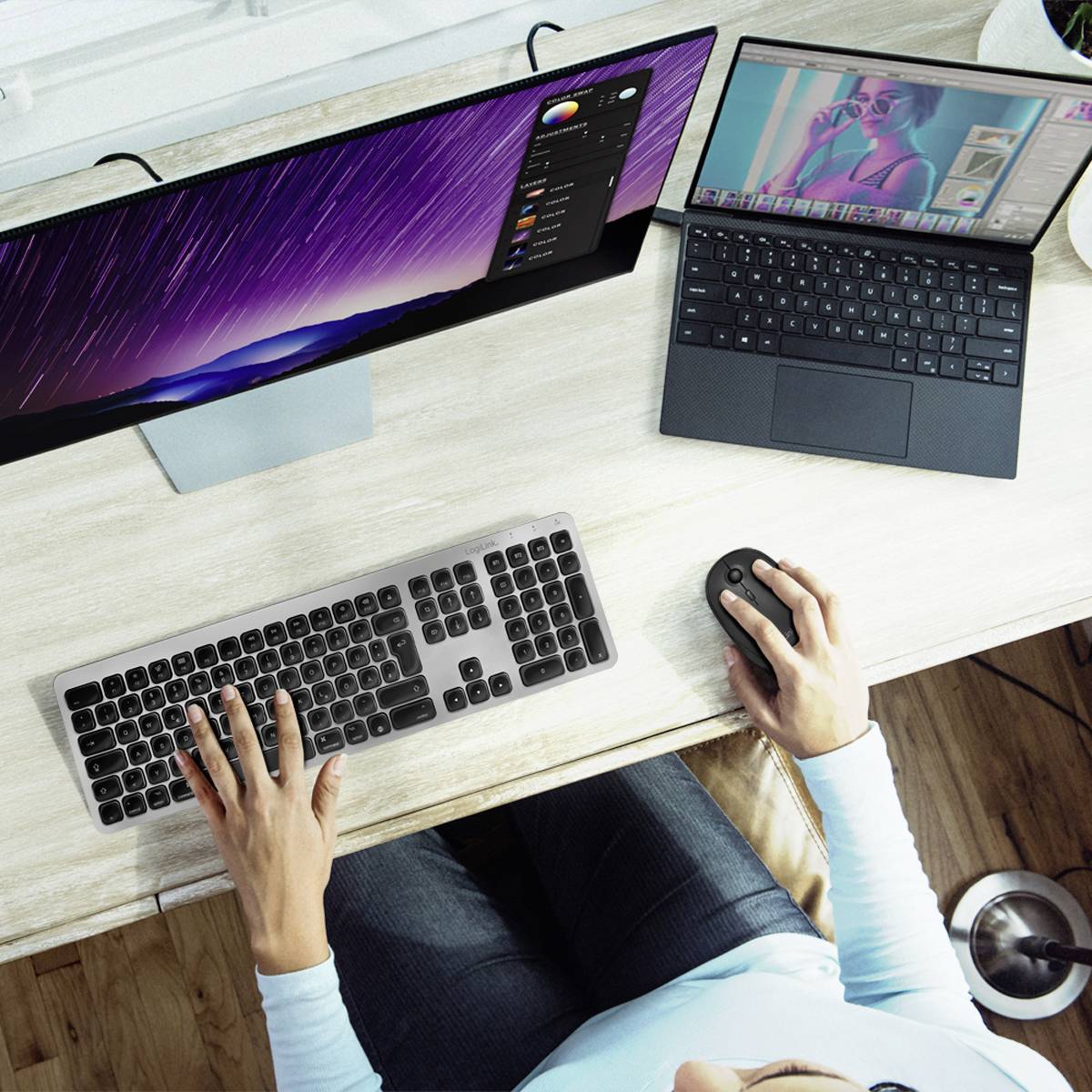 Die Person arbeitet an einem Tisch mit zwei Monitoren. Einer zeigt Farbänderungen, der andere zeigt ein Bildbearbeitungsprogramm.