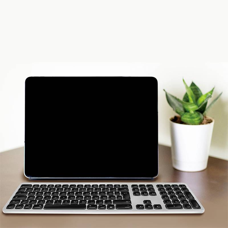 'Ein Laptop mit schwarzem Bildschirm steht auf einem Tisch neben einer kleinen Pflanze und einer kabellosen Tastatur.'