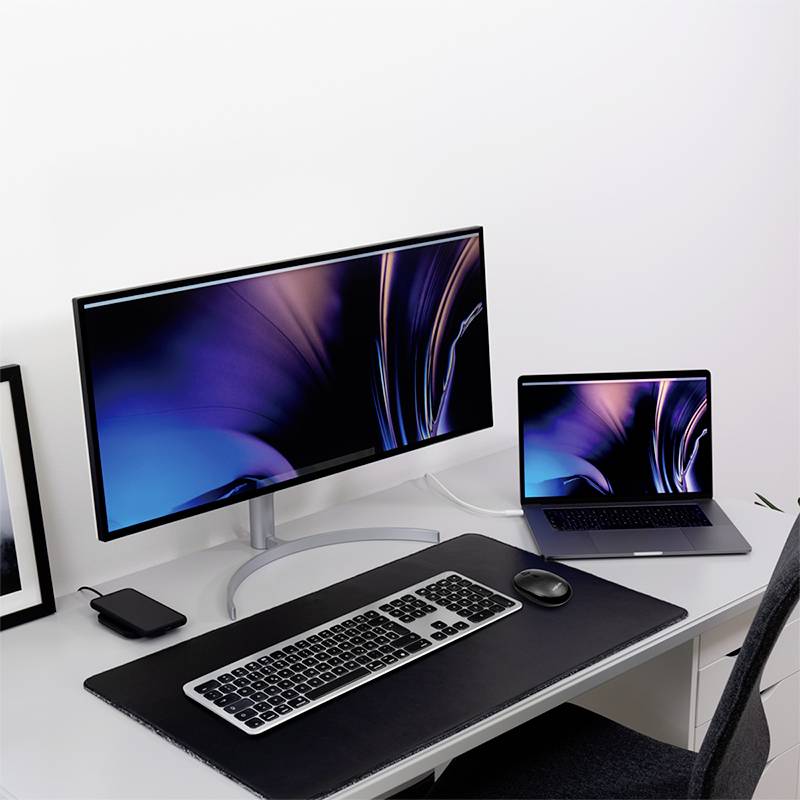 Ein Schreibtisch mit einem Monitor und einem Laptop, beide mit einem futuristischen Bildschirmhintergrund. Neben dem Laptop liegt eine Maus.