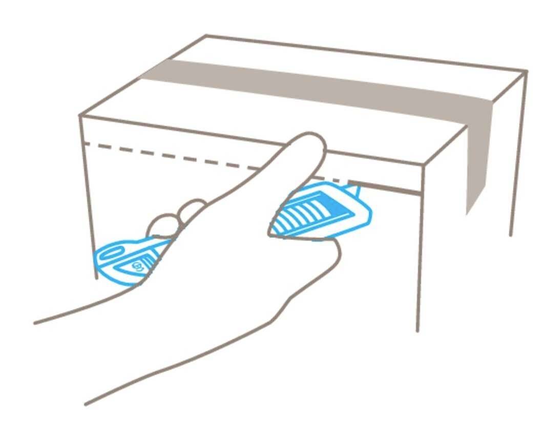 Eine Hand schiebt ein blaues, rechteckiges Objekt in einen schlitzartigen Eingang an der Seite eines Pappkartons.