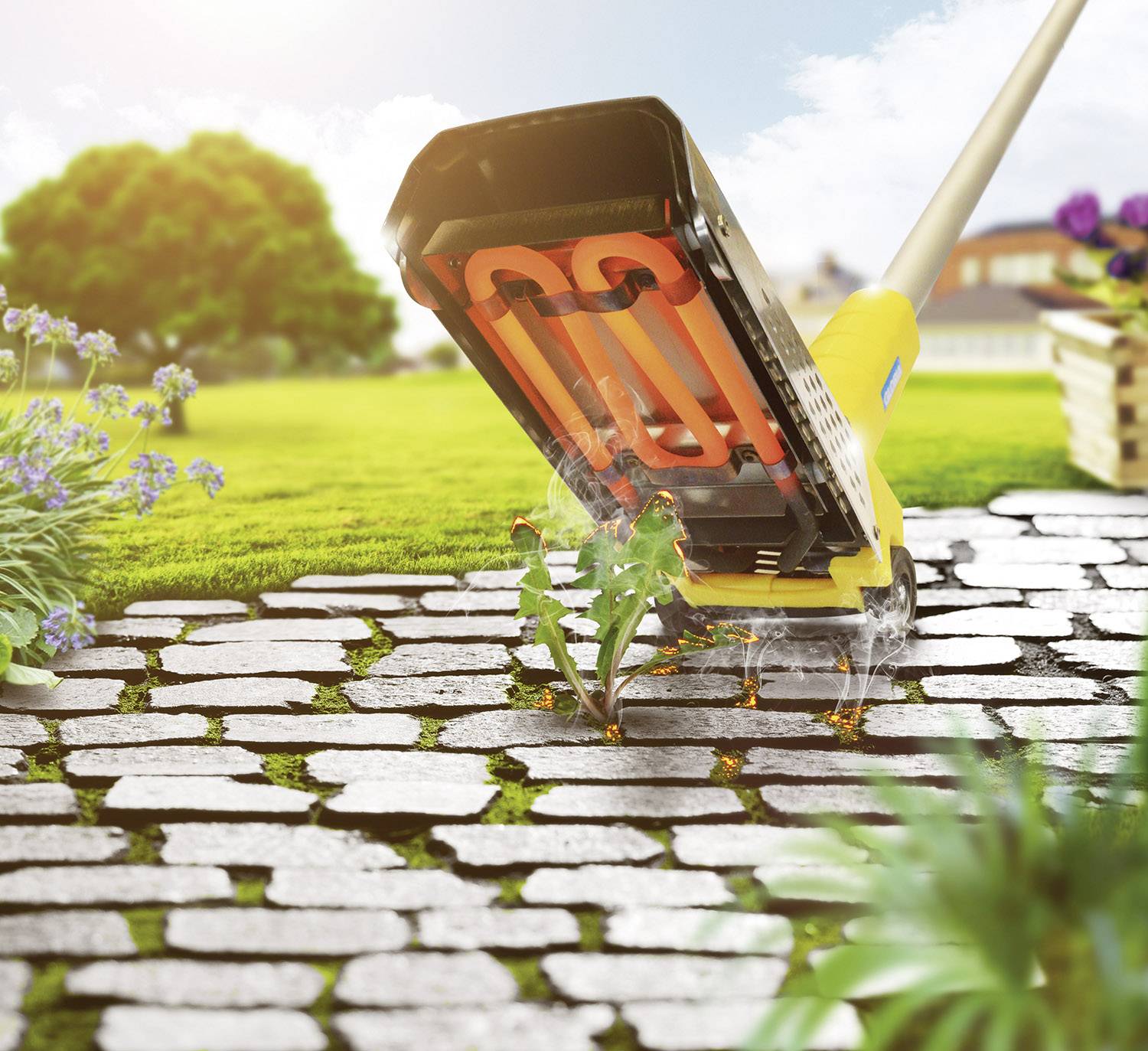 Eine Unkrautbürste entfernt Unkraut zwischen Pflastersteinen in einem sonnigen Garten. Im Hintergrund sind Blumenbeete und Bäume.