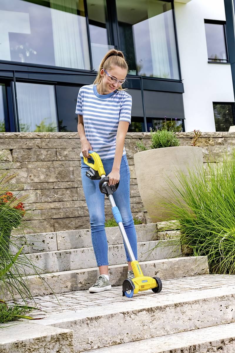 Eine Person benutzt einen handgehaltenen Reinigungsgerät für Treppen im Freien. Im Hintergrund ein modernes Haus mit großen Fenstern.