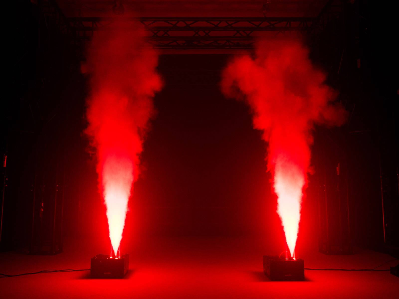 Zwei Lichtmaschinen erzeugen hohe rote Strahlen, die nach oben gerichtet sind, auf einer dunklen Bühne.