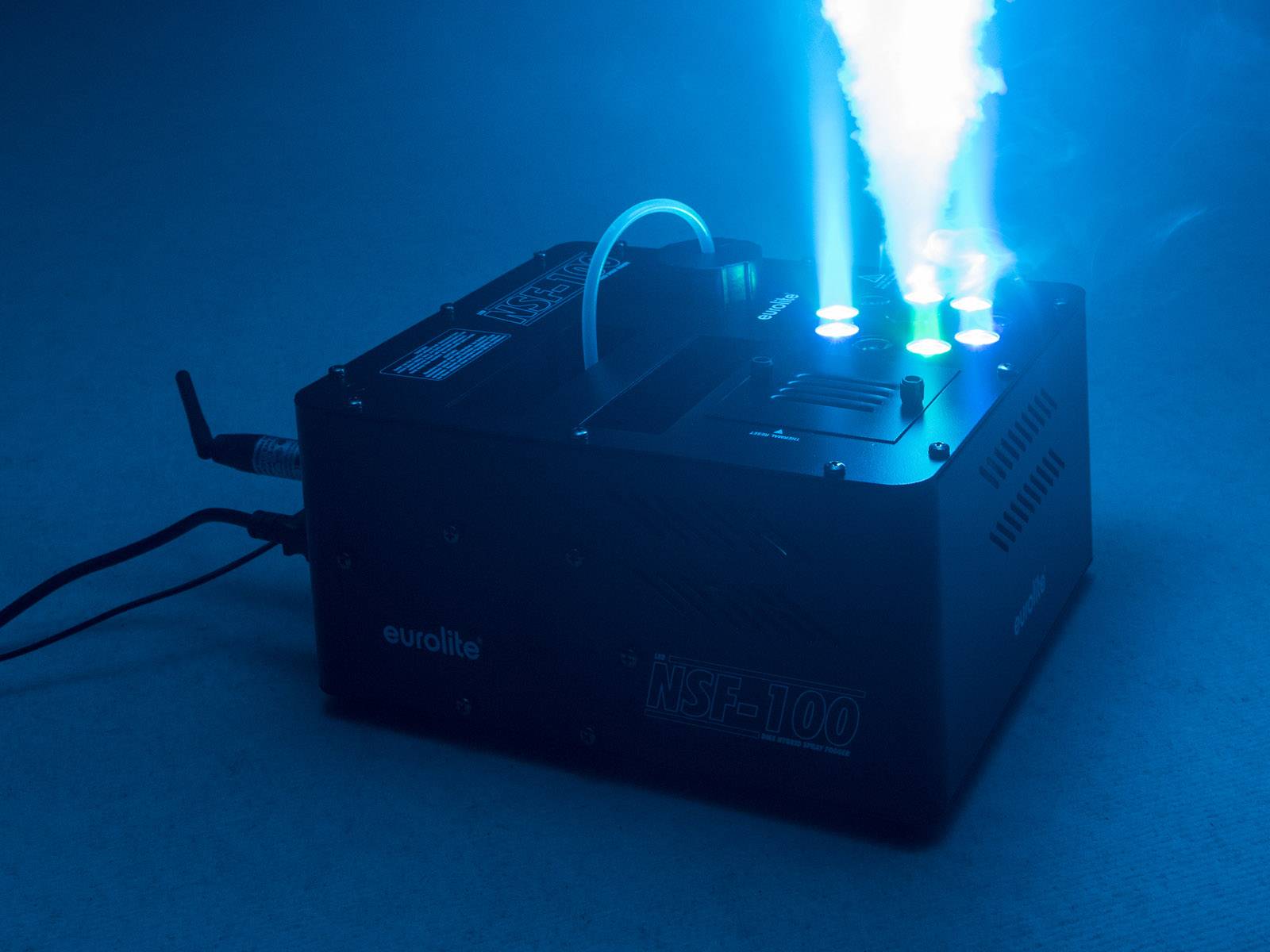 'Nebelmaschine sprüht blauen Nebel in einem dunklen Raum. Lichtstrahlen und Rauch erzeugen eine futuristische Atmosphäre.'