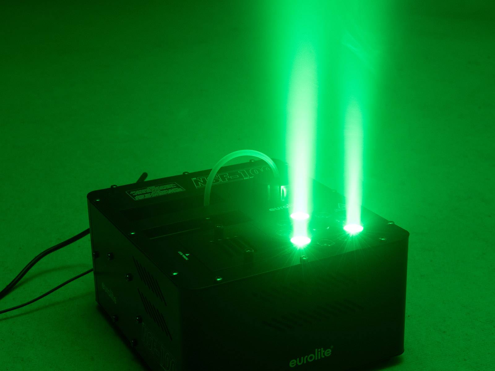 Ein schwarzer Projektor strahlt zwei helle, grüne Lichtstrahlen in einem dunklen Raum aus.