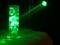Ein Glaszylinder mit Eiswürfeln wird von einem grünen Lichtstrahl beleuchtet, wodurch die Eiswürfel leuchten.