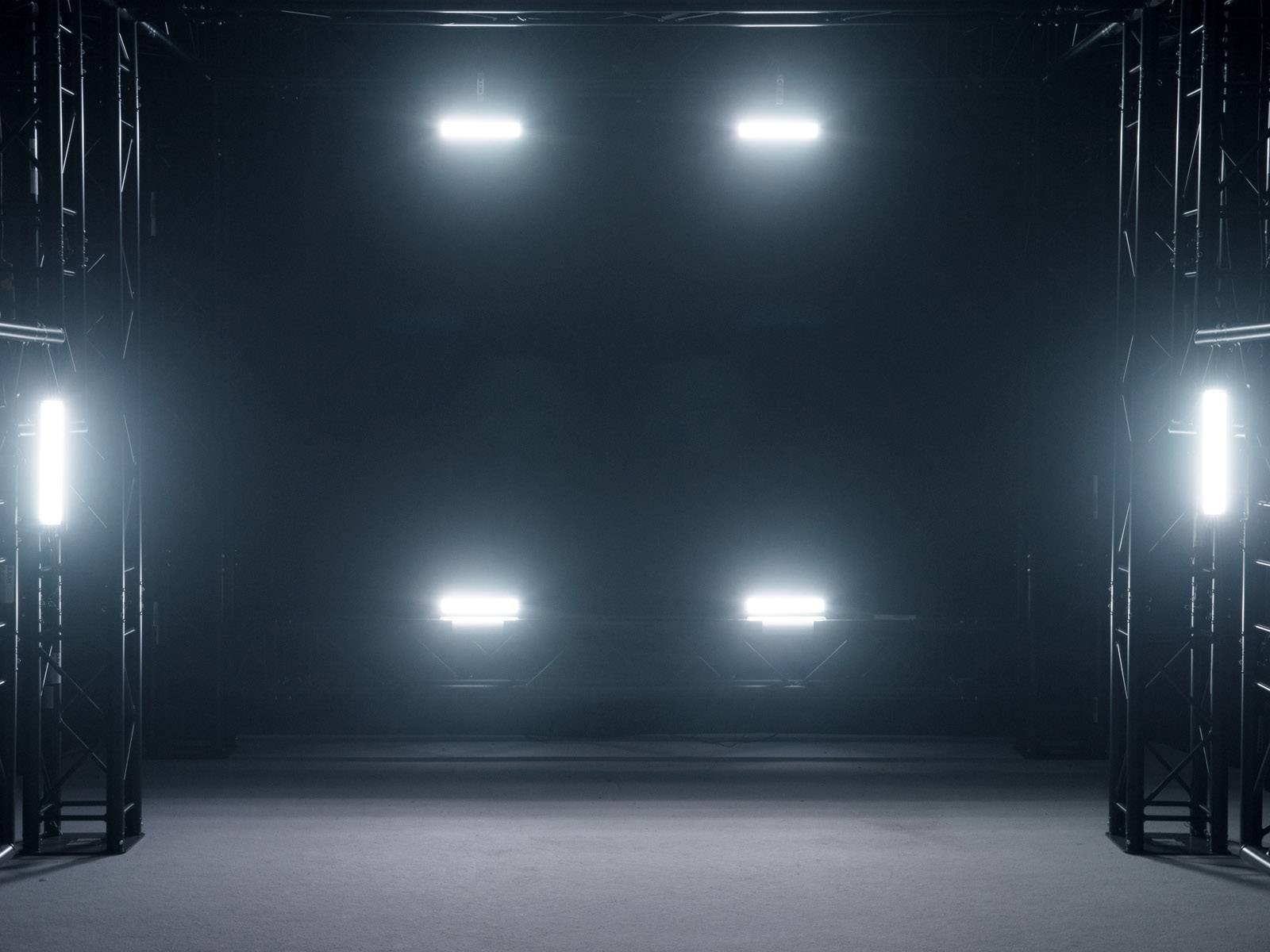 Lichter richten sich in einem dunklen Raum aus, um eine Bühne zu beleuchten. Metallstrukturen umgeben den Raum.