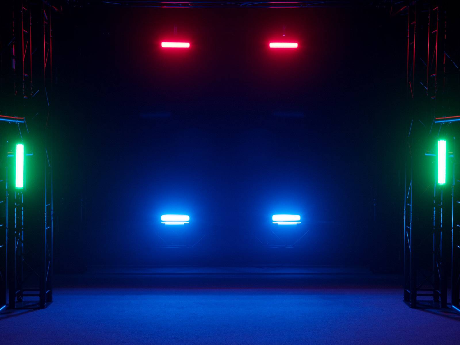 Eine dunkle Bühne mit sechs leuchtenden Lichtern: zwei rote oben, zwei blaue unten und zwei grüne an den Seiten, die eine futuristische Atmosphäre erzeugen.