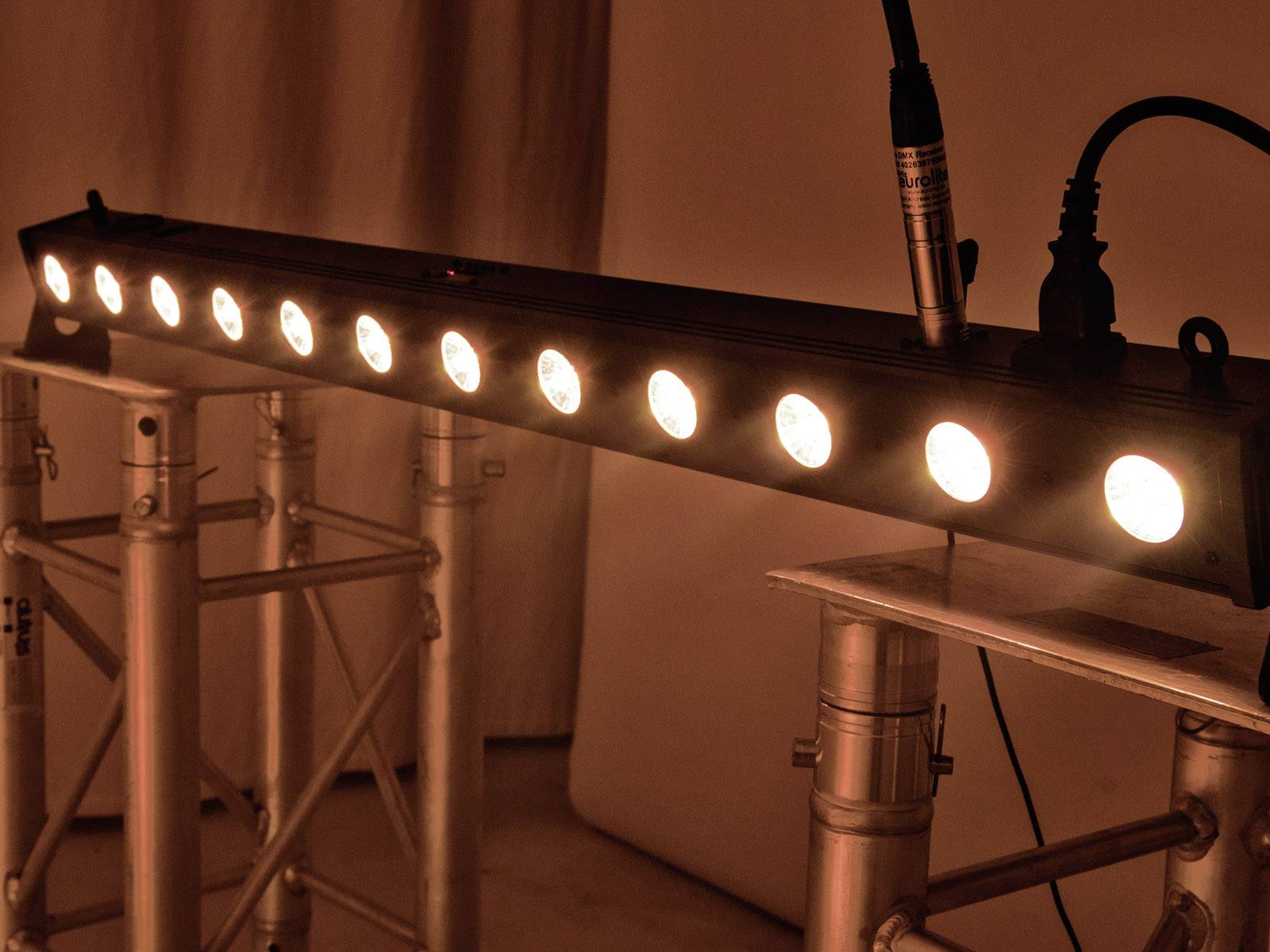 Eine LED-Lichtleiste auf einem Gerüst beleuchtet, wobei mehrere runde Lichter sichtbar sind. Sie wird von Kabeln an der Oberseite versorgt.