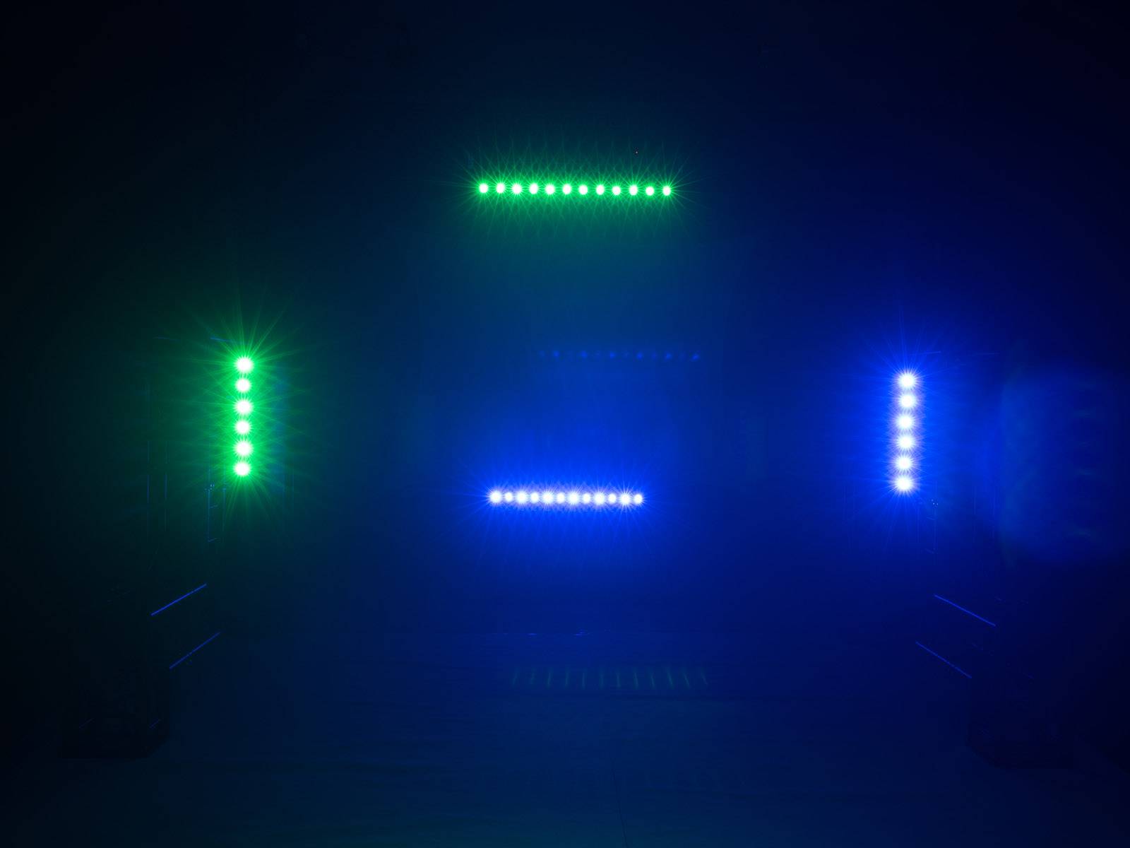 Bunte Lichter in Grün und Blau leuchten in einem dunklen Raum, angeordnet in horizontalen und vertikalen Linien, erzeugen ein geometrisches Muster.