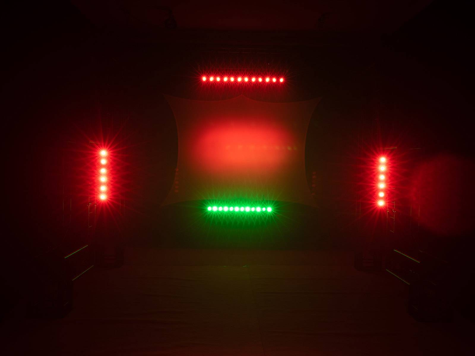 Ein dunkler Raum beleuchtet mit roten und grünen LED-Lichtern, die auf eine Leinwand gerichtet sind, erzeugt eine stimmungsvolle Atmosphäre.