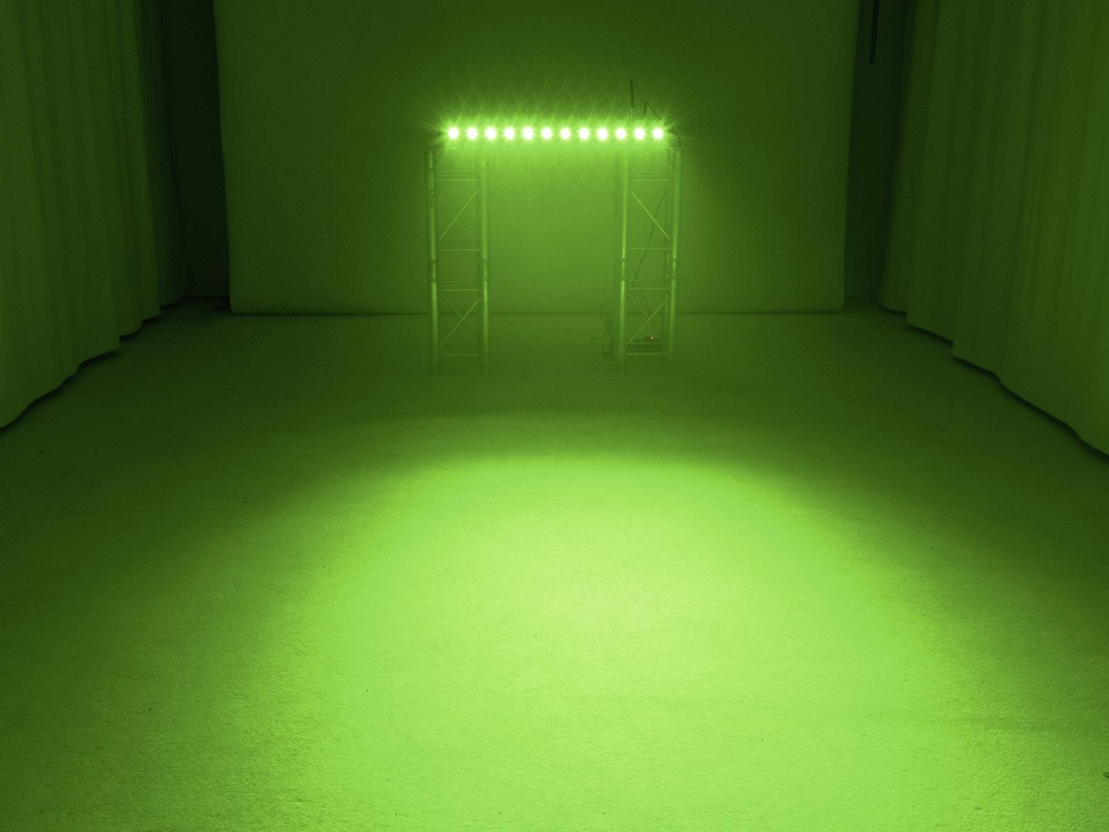 Ein Raum mit grünem Licht, das von oben auf eine strukturierte Fläche beleuchtet wird. Im Hintergrund ist ein Metallrahmen sichtbar.