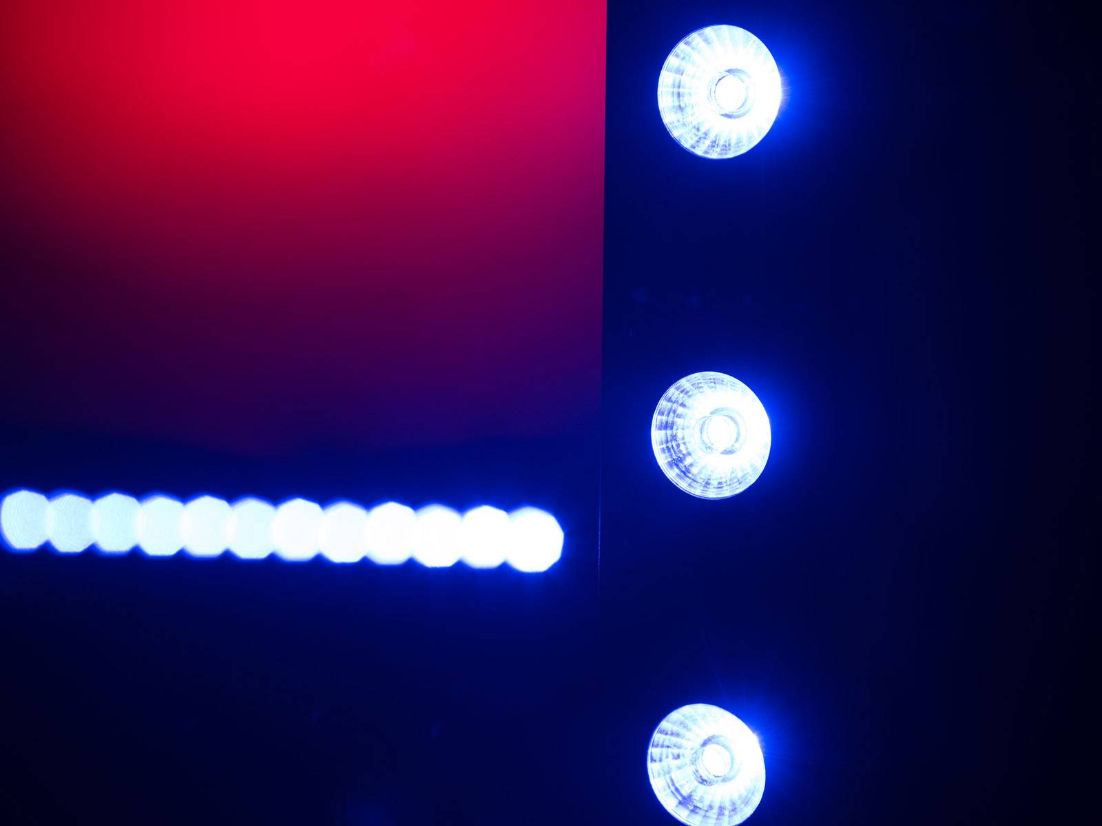 'Drei blaue Lichter senkrecht neben einer Reihe horizontaler blauer Lichter, auf einem schwarzen Hintergrund mit roter Ecke.'