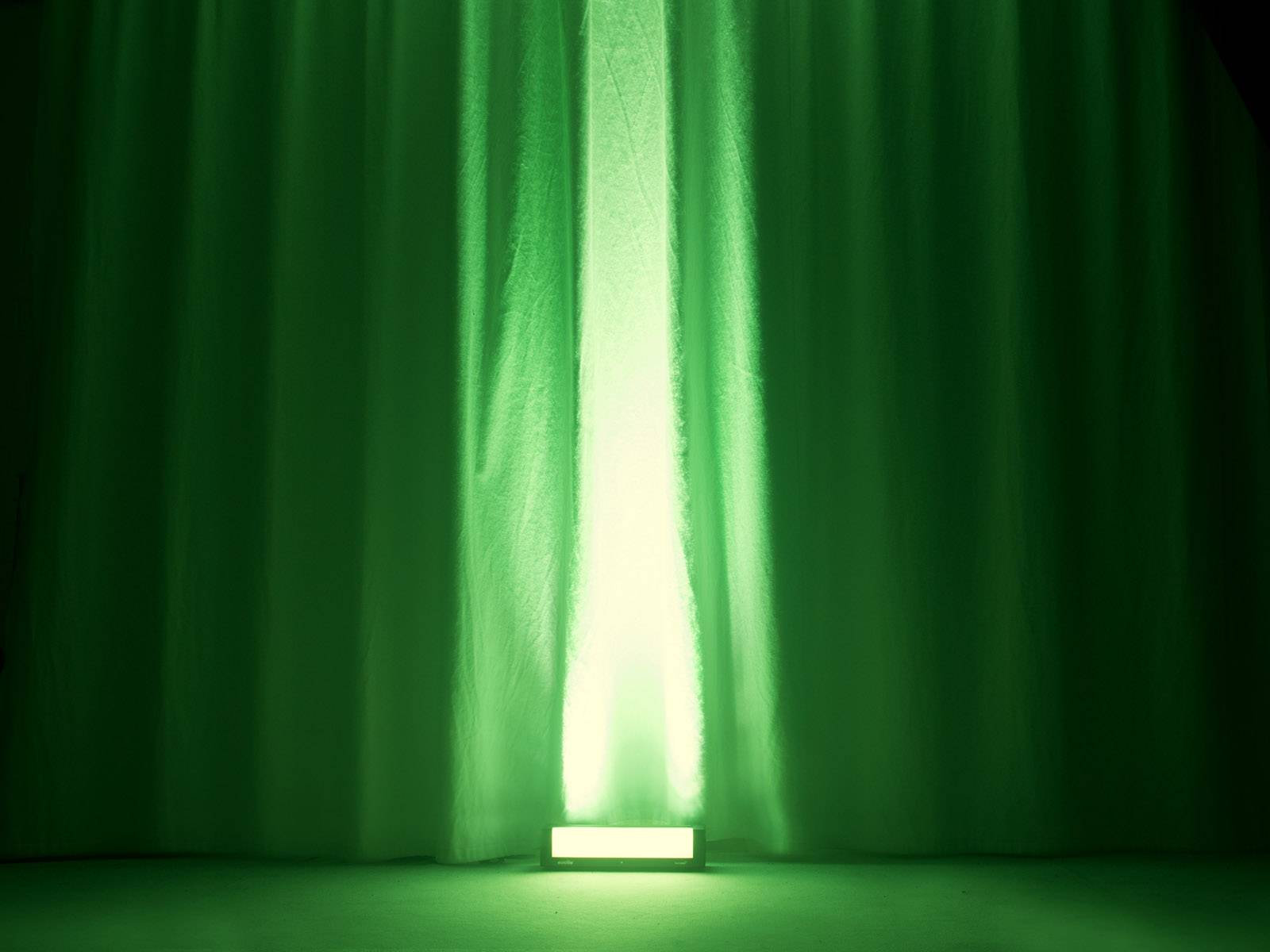 Ein grüner Vorhang, der von unten angestrahlt wird. Die Beleuchtung erzeugt einen intensiven Lichteffekt auf dem Stoff.