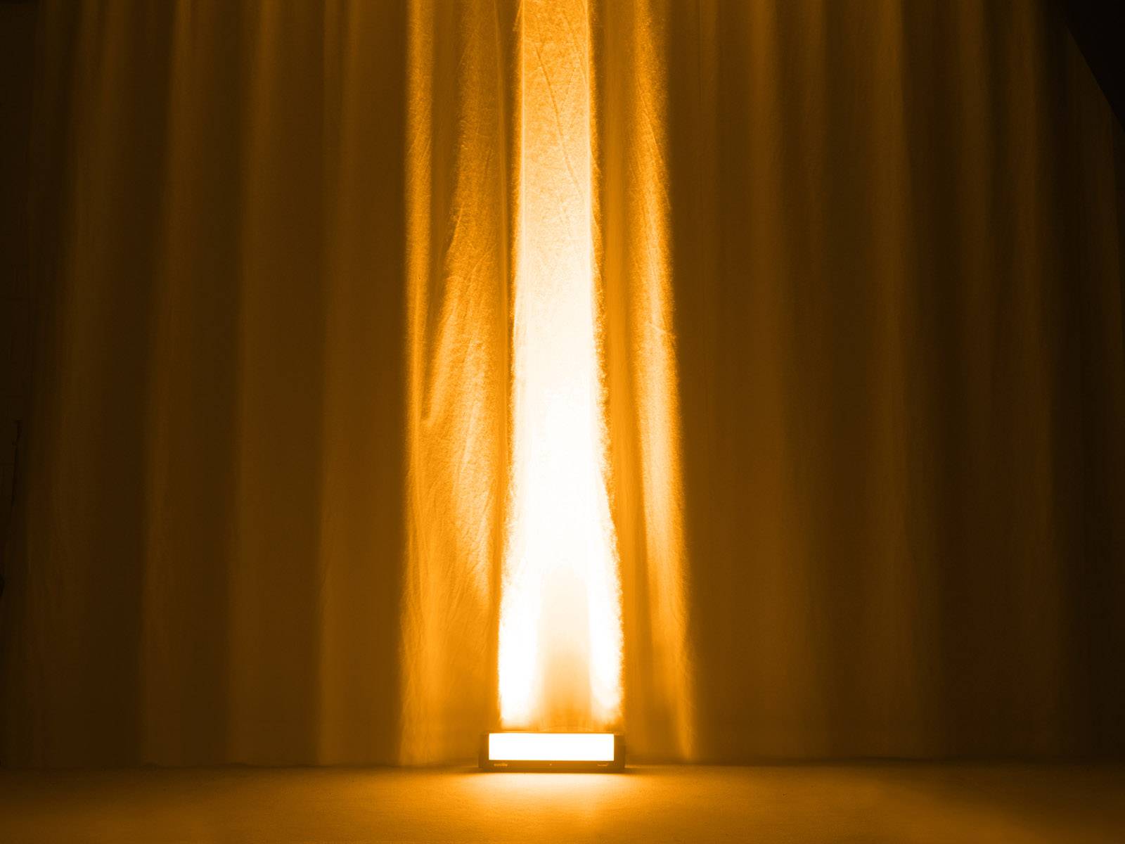 Ein Vorhang mit gelbem Lichtstrahl, der von unten nach oben leuchtet, erhellt die Raumstimmung warm und gleichmäßig.