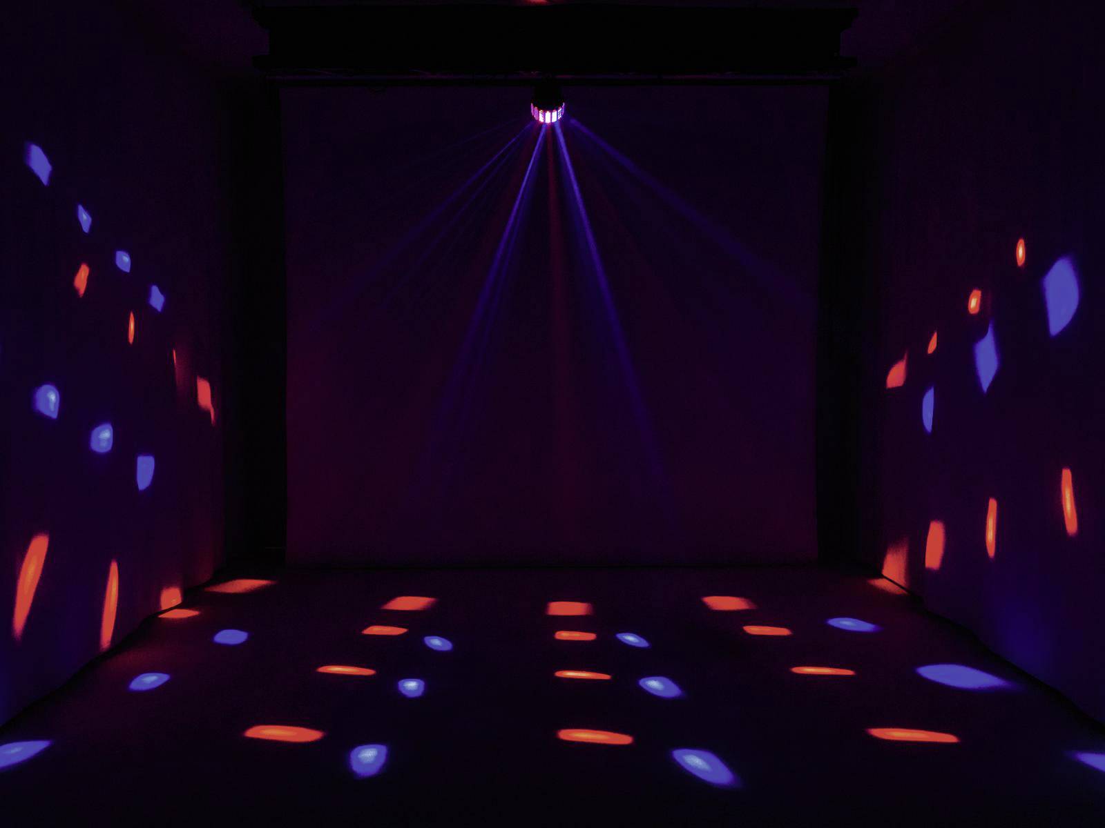 Bunte Lichtmuster werden in einem dunkel beleuchteten Raum an Wände und Boden projiziert, was eine lebhafte Atmosphäre schafft.