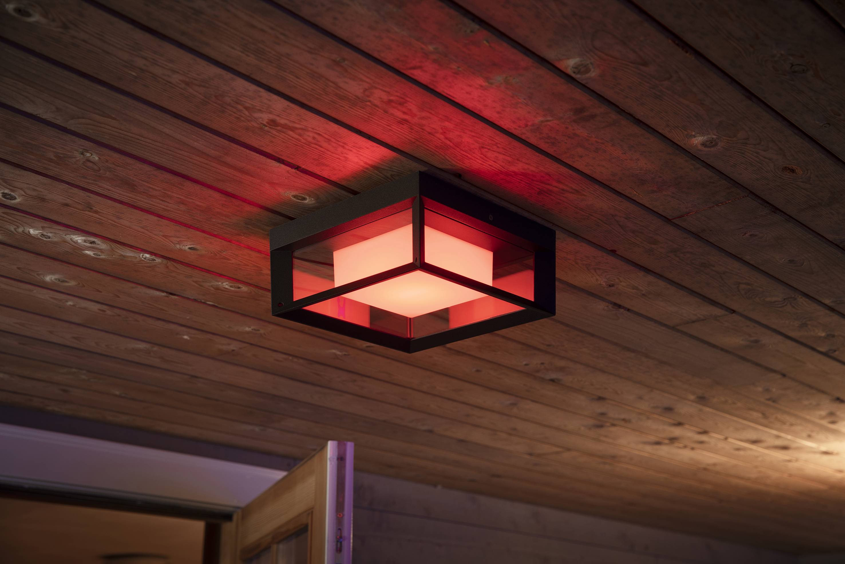 Eine rote Deckenleuchte aus Metall und Glas hängt an einer Holzdecke. Sie beleuchtet subtil den Raum und erzeugt eine warme Atmosphäre.