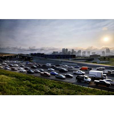 Dichter Verkehr auf einer Autobahn bei Sonnenuntergang, mit einer Stadt und Hochhäusern im Hintergrund. Hauptsächlich Autos und LKWs.