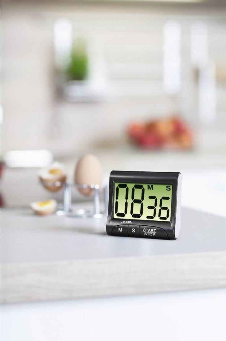 Ein digitaler Küchentimer zeigt '08:36', im Hintergrund ein weich gekochtes Ei, unscharfe Küchenelemente im Hintergrund.