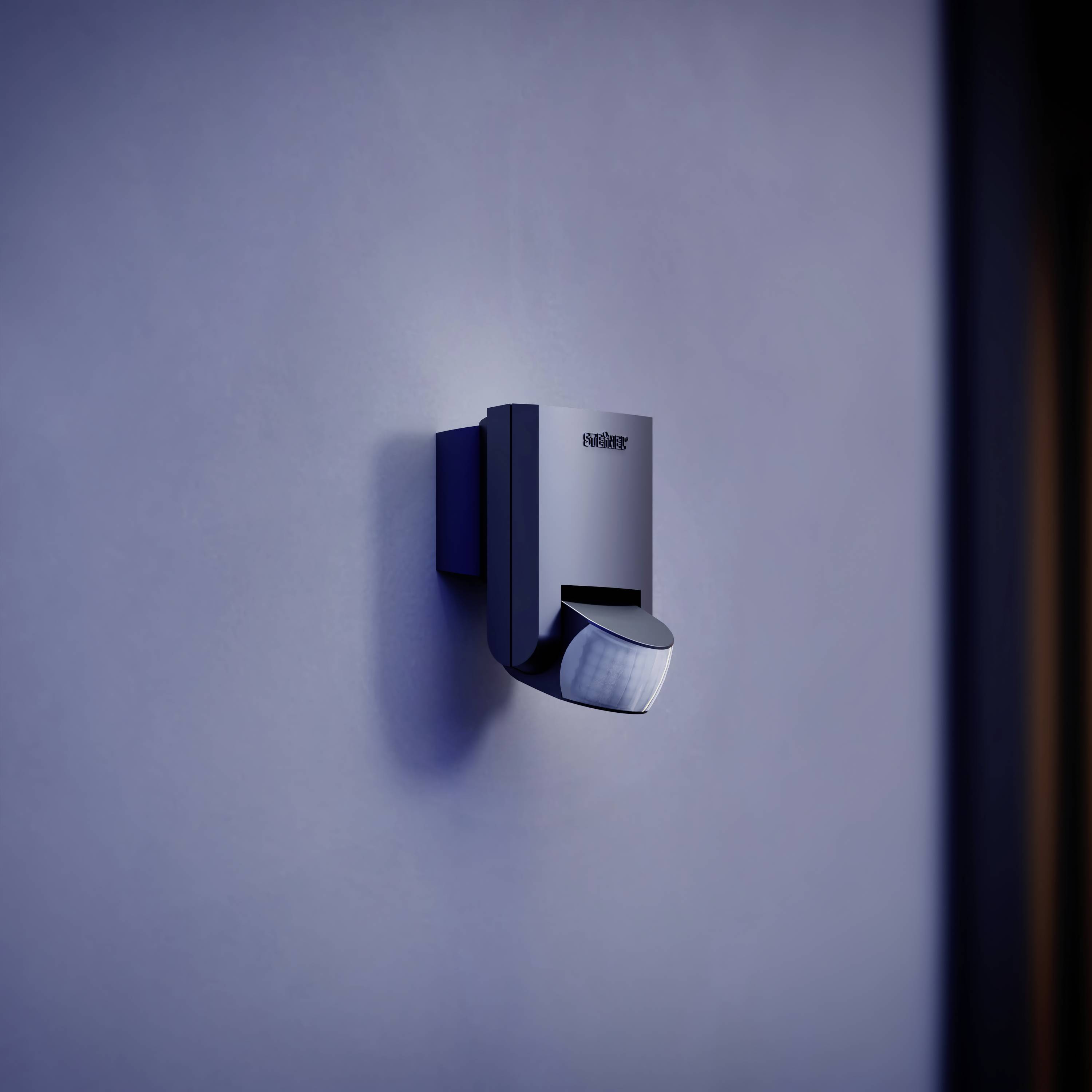 Ein Bewegungsmelder mit dunklem Gehäuse ist an einer blauen Wand montiert, beleuchtet von schwachem Licht.