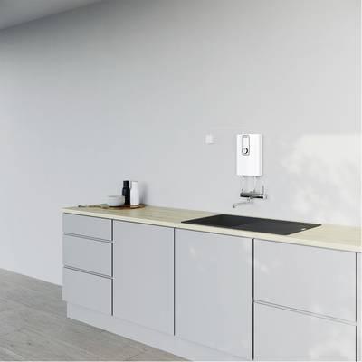 Eine minimalistische Küchenecke mit grauen Schränken, einer Holzarbeitsplatte, einem Elektroherd, einem Wasserkocher und einer weißen Wand.