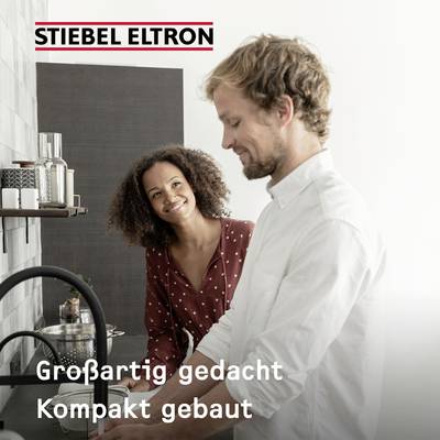 Ein Mann und eine Frau stehen lächelnd in einer modernen Küche nebeneinander. Text oben: 'STIEBEL ELTRON', unten: 'Großartig gedacht, Kompakt gebaut'.