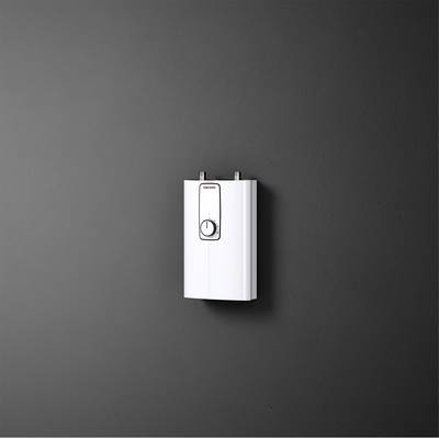 Ein moderner, wandmontierter elektrischer Durchlauferhitzer mit einem zentralen Drehknopf befindet sich vor einer grauen Wand.