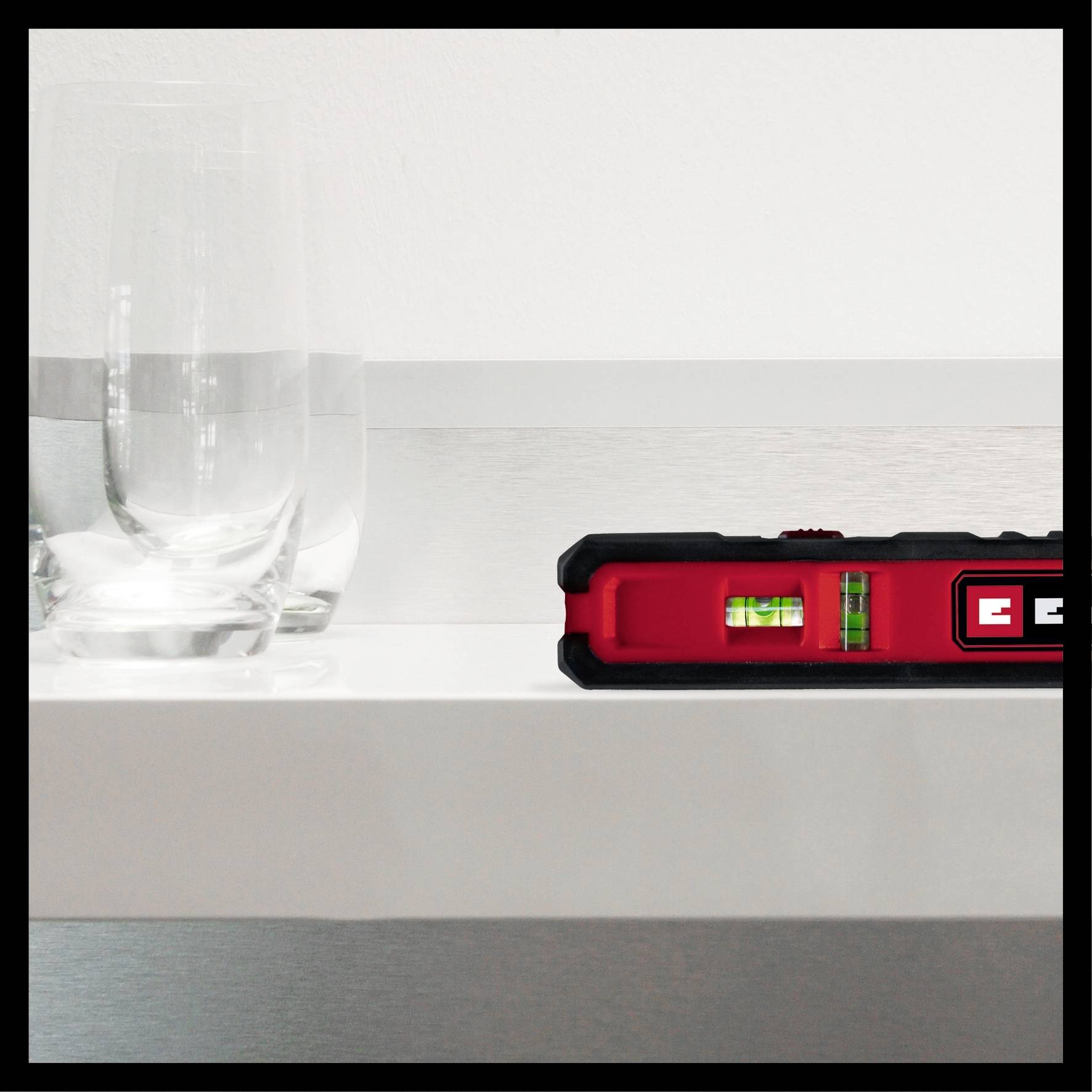 Ein rotes Wasserwaagenwerkzeug zeigt eine perfekte Ausrichtung auf einem weißen Regal. Links ein halb volles Glas Wasser.