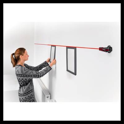 Eine Frau hängt mit Hilfe eines Lasernivelliergeräts zwei Bilder an einer weißen Wand auf.