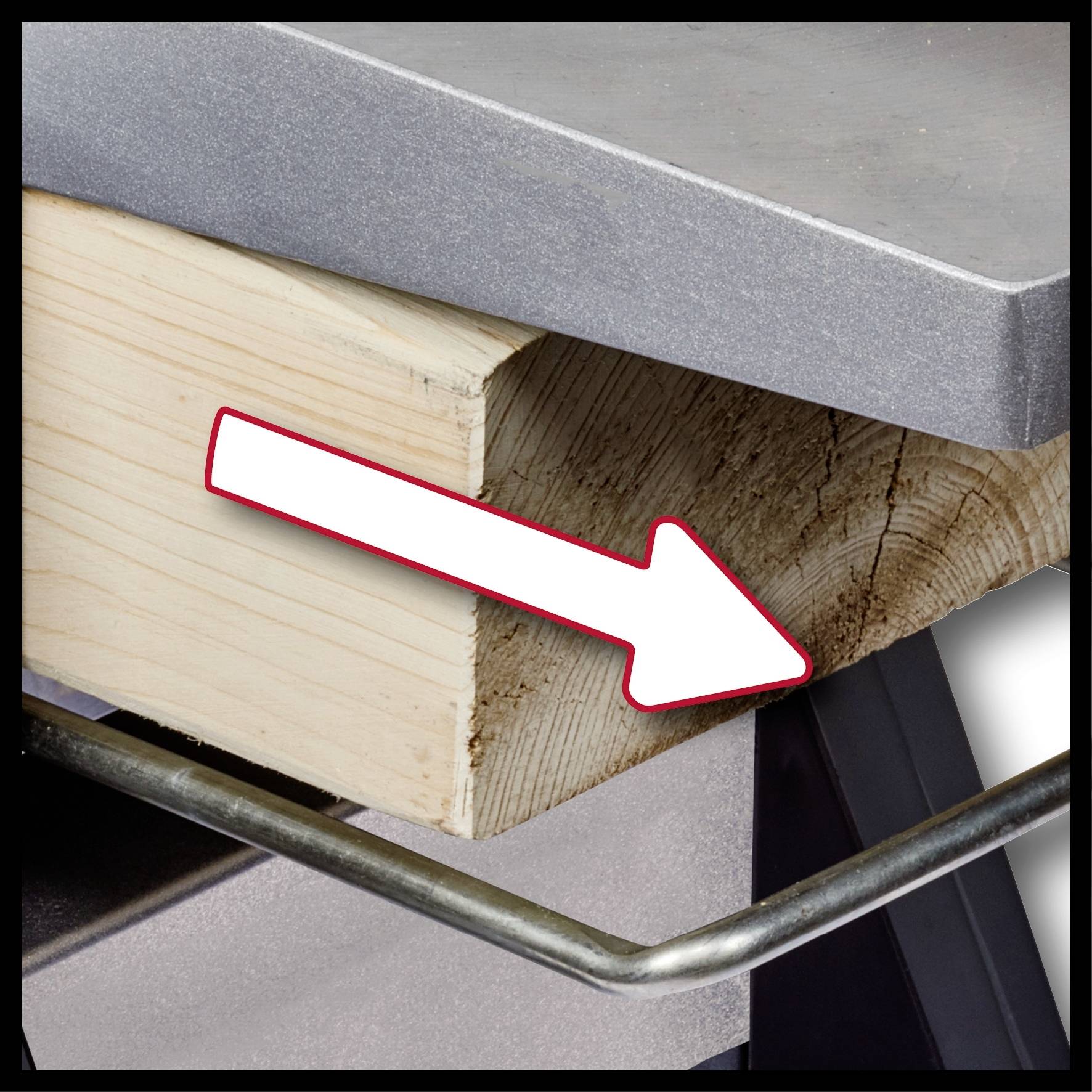 Ein Holzblock mit diagonaler Schnittkante stützt eine Metallplatte, auf die mit einem weißen Pfeil von links nach rechts gezeigt wird.