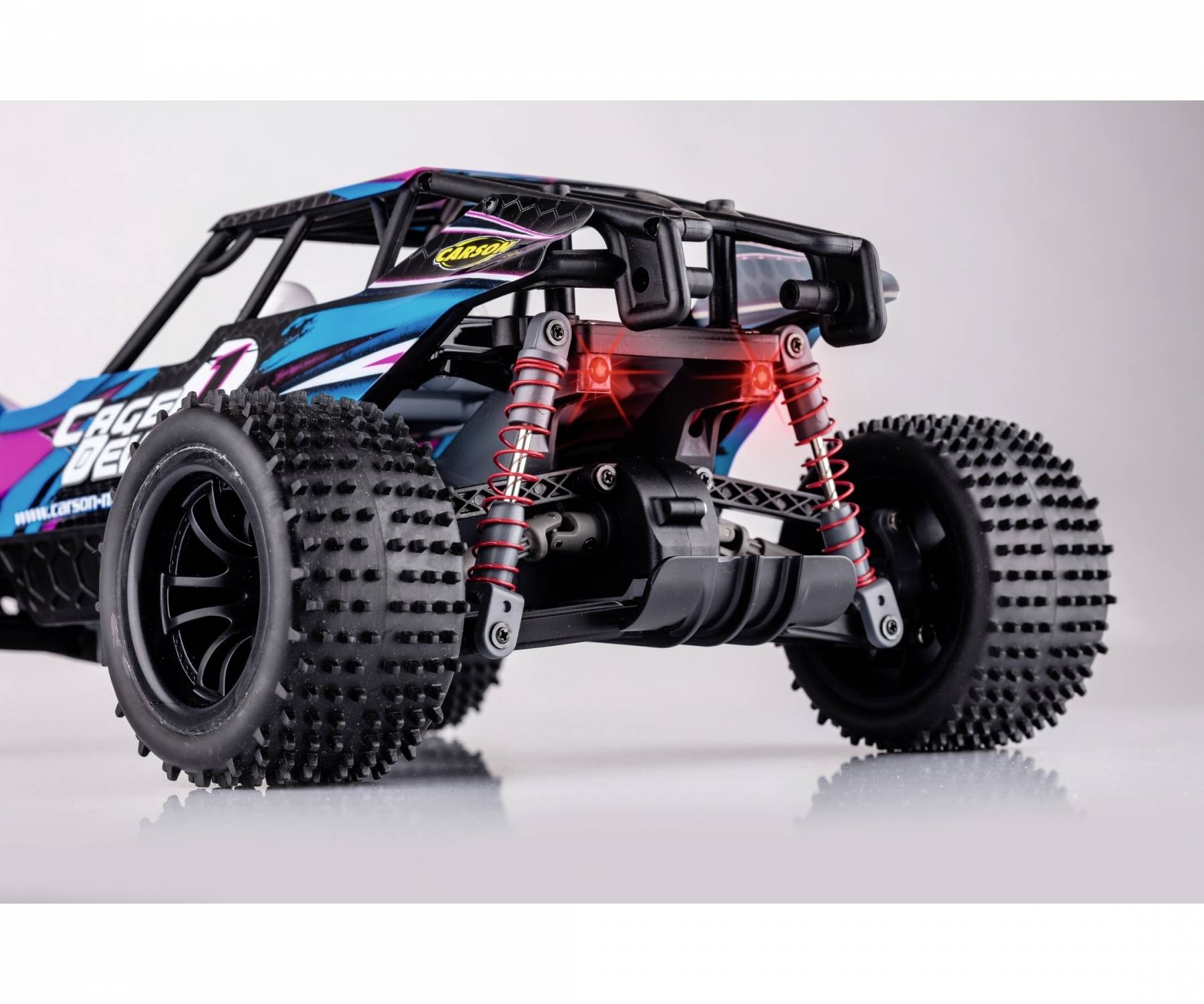 Spielzeug-Buggy mit grobstolligen Reifen und rot gefederten Stoßdämpfern auf hellgrauem Hintergrund.
