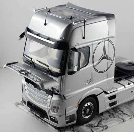 Silberner Lastwagen mit Mercedes-Logo, vordere Haube geöffnet, auf grauem Hintergrund.