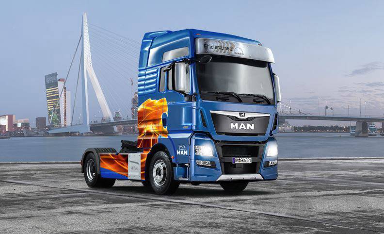 Blauer MAN-Lkw ohne Anhänger steht auf einem Stadtplatz mit modernem Architekturhintergrund und Brücke, bewölkter Himmel.