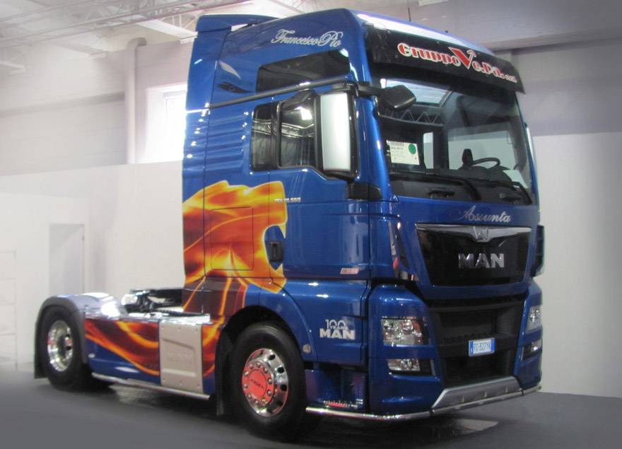 Ein blauer LKW mit auffälligem Flammen-Design an der Seite steht in einer Halle. Der Schriftzug 'Grampan G. Dodino' ist oben sichtbar.