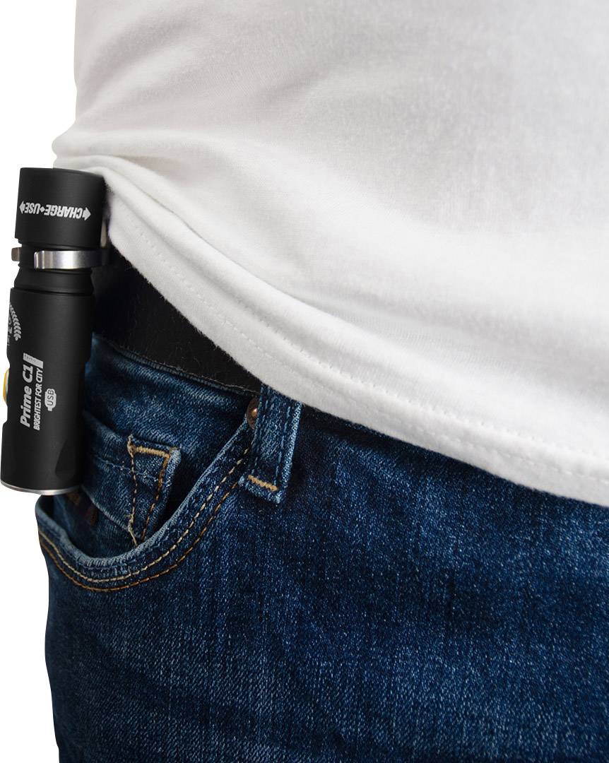 Eine kleine Taschenlampe ist am Hosenbund einer blauen Jeans befestigt. Sie steckt leicht in der Hosentasche eines weißen T-Shirts tragenden Menschen.