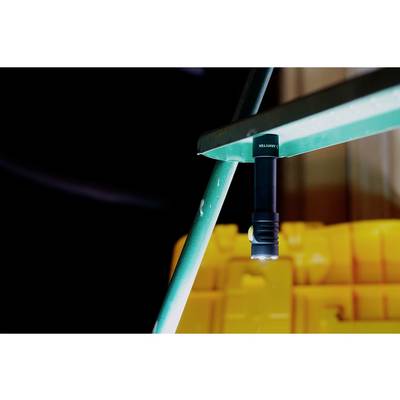 Eine schwarze Taschenlampe ist magnetisch an einem grünen Metallregal befestigt, Hintergrund unscharf mit gelbem Behälter.