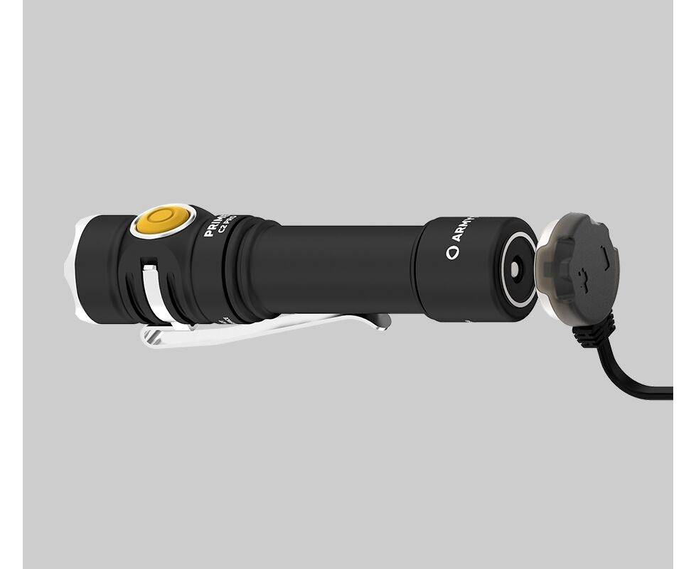 Schwarze Taschenlampe mit gelbem Knopf und Metallclip liegt waagerecht. Ein rundes Ladegerät ist an der Rückseite angeschlossen.