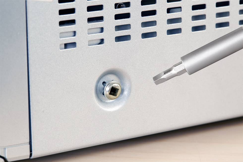 Ein Schraubendreher wird vor eine Schraube an einem silbernen Gehäuse positioniert, bereit zum Anziehen oder Lösen der Schraube.