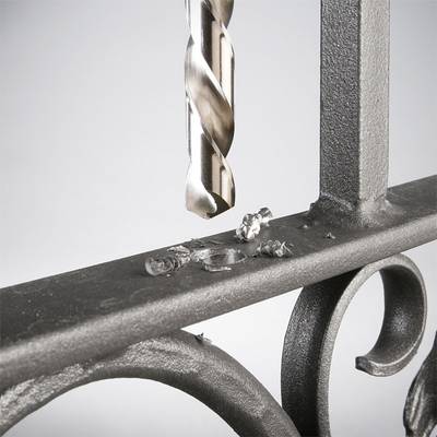 Ein Bohrer durchbohrt einen Metallzaun, Metallspäne liegen auf der Oberfläche.