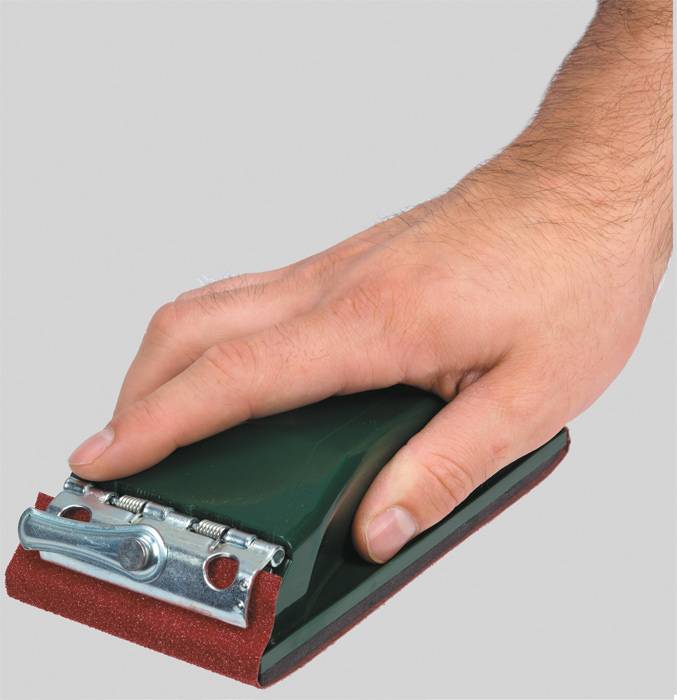 Eine Hand hält ein Schleifgerät mit rotem Schleifpapier unten.