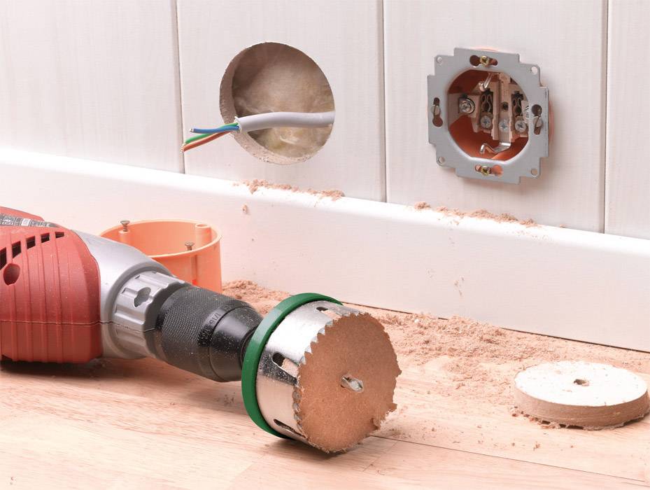 Eine Bohrmaschine liegt auf dem Boden neben einer Wand mit einer vorbereiteten Bohrstelle und einer unvollständigen Steckdose.