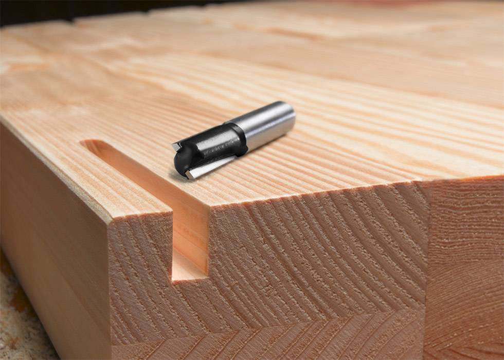Ein Holzstück mit präzise gefräster Nut und Fräswerkzeug daneben, zeigt Handwerkskunst und maschinelle Präzision im Tischlerhandwerk.