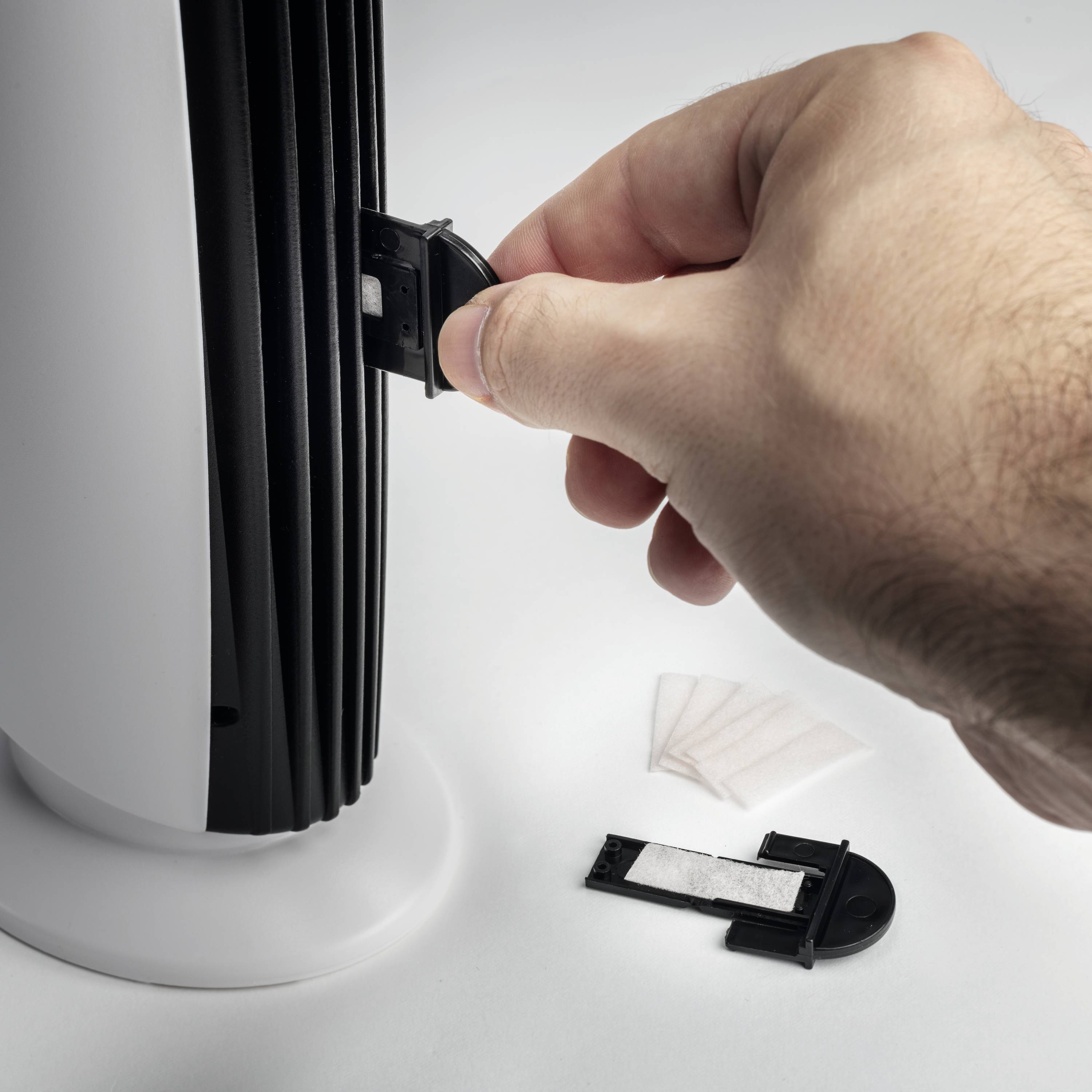 Eine Hand öffnet das Batteriefach eines elektrischen Geräts. Daneben liegen eine Batterieabdeckung und Batterien auf einer Oberfläche.