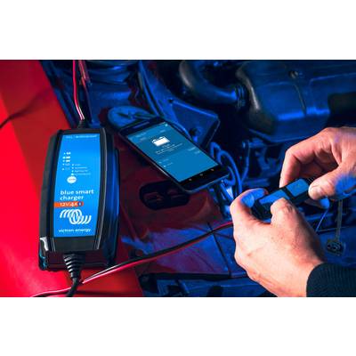 'Ein Ladegerät wird an eine Autobatterie angeschlossen, mit einem Smartphone-Display, das den Ladevorgang überwacht.'