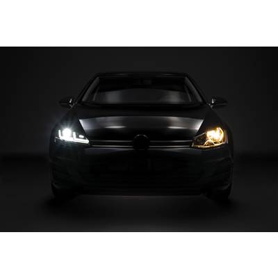 Ein schwarzes Auto in einer dunklen Umgebung mit eingeschaltetem Abblendlicht auf der linken Seite und Fernlicht auf der rechten Seite.
